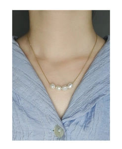 Close-up of natural baroque pearls on a gold chain necklace worn over a blue shirt