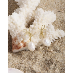 Elegant gold bow earrings with baroque pearls on white coral beach background