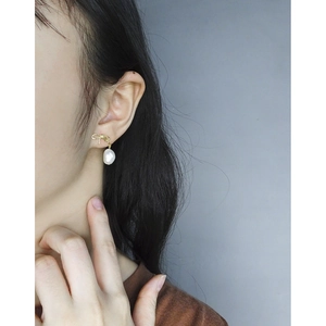 Baroque pearl drop earrings with gold bow design shown on a model's ear in high detail