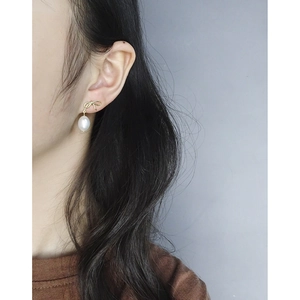 Elegant gold bow earrings with baroque pearl drop pendant worn by a model