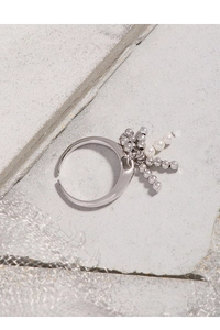 Detail of adjustable silver S925 ring with white pearl and bead charms on stone background
