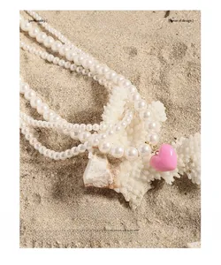 Detail of multi-layer pearl necklace with pink heart pendant on a beach coral background