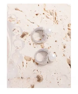 Close-up of minimalist silver wide hoop earrings with white pearls on stone surface