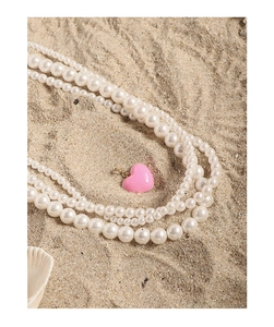 Close-up of pink heart pendant on multi-layer pearl necklace over beach sand