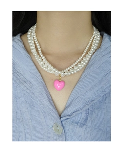 Detail view of a triple-layer pearl choker with a pink heart pendant on model
