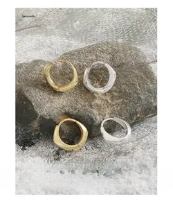 Irregular geometric hoop earrings in gold and silver finish on dark rock surface