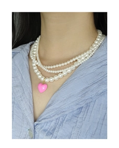 Close-up of triple-layered pearl necklace with a pink heart pendant on a model