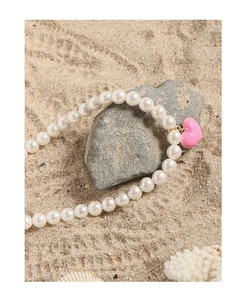 Pink heart pendant with white pearls on a beach setting with shells and coral