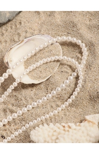 Detail of elegant white pearl necklace with pink heart pendant on beach sand background