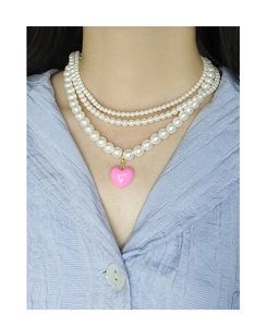Detailed close-up of triple-layered pearl necklace with a pink heart pendant on a shirt