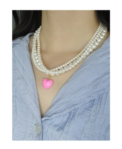 Detail of triple-layer pearl necklace featuring a pink heart pendant on model