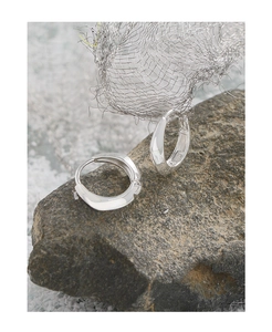 Macro detail of silver S925 hoop earrings with irregular edges on a grey rock background