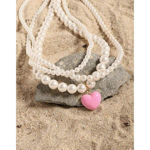 Multi-layer pearl necklace with a pink heart pendant on a natural stone beach background