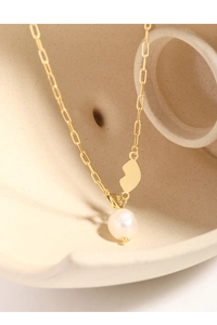 Macro detail of a gold heart pendant and lustrous baroque pearl on a paperclip chain