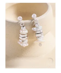 Macro shot of long drop earrings with silver beads and irregular baroque pearls on a ceramic cup