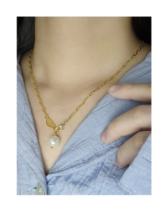 Close-up of golden paperclip chain necklace with pearl pendant and heart clasp on model