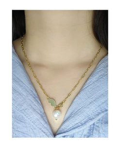 Close-up of gold paperclip chain necklace with round pearl and heart pendant on a model