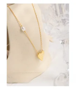 Close-up of a gold necklace featuring a textured heart pendant and water-drop pearl detail