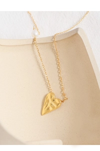 Macro detail of a brushed gold heart pendant with a white pearl on a fine chain