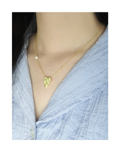 Close-up of gold crumpled heart pendant necklace with white pearl on a female model