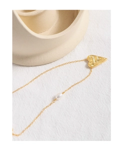 Detailed close-up of a gold hammered heart pendant with a white pearl on a fine chain