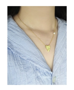 Detail of gold textured heart pendant necklace with pearl on elegant silk shirt