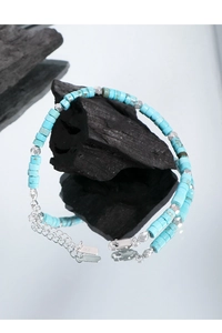 Macro detail of S925 silver stamp on turquoise beaded bracelet over charcoal