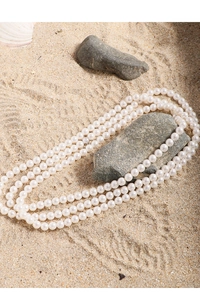 Detailed view of layered white pearl necklaces on a sandy beach with natural shells
