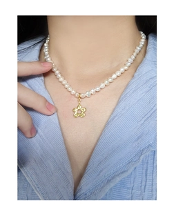 Detail view of Baroque pearl necklace with a golden flower pendant on model's neckline