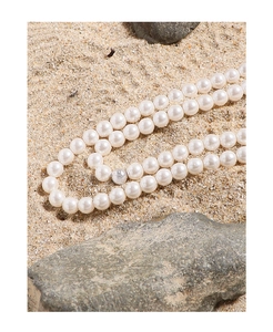 Detail of double-layer pearl necklace on sand with silver accents and elegant luster