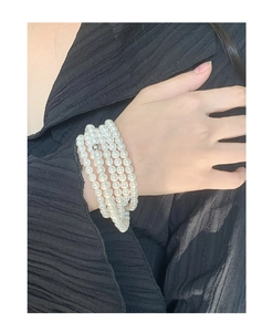 Detail of multi-layer 5-6mm white pearl strand bracelet on black textured fabric