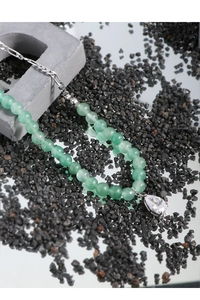 Detail of green aventurine beaded necklace with water drop zircon pendant on mineral rocks