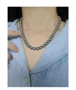 Close-up of minimalist grey pearl necklace with metallic luster on blue striped shirt