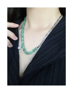 Detail of green aventurine bead necklace and silver Figaro chain on a black background