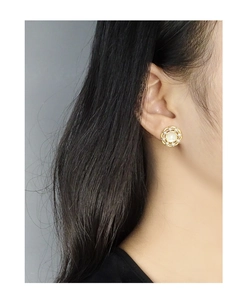 Gros plan de boucles d'oreilles couronne en nacre et argent S925 portées par un mannequin