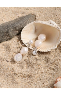 Close-up of three baroque pearls on beach sand with shell and rock backdrop