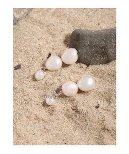 Detail of natural baroque pearl earrings on sand with silver metal connectors