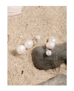 Macro shot of natural Baroque freshwater pearl earrings on sand with silver studs