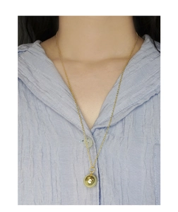 Primer plano de un collar largo minimalista de plata S925 con colgante de bola dorada pulida
