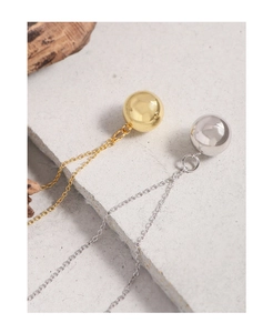 Primer plano de colgantes de bolas minimalistas en oro y plata sobre una piedra gris