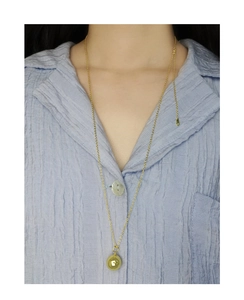 Collar de cadena con bola dorada minimalista sobre camisa plisada azul claro