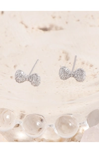 Close-up of bow-shaped S925 silver earrings with pavé cubic zirconia on glass tray