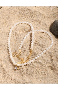 Close-up of pearl necklace with gold clasp and zircon pendant on a sand background
