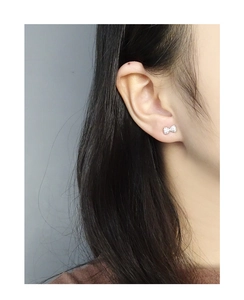 Close-up of minimalist bow stud earrings with sparkling zircons worn on ear