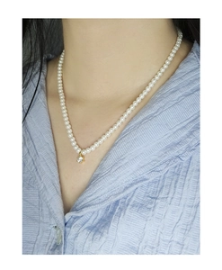 Detail view of a pearl necklace with a central gold-set zircon on a blue shirt