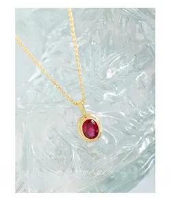 Detail of a gold S925 necklace with an oval red zircon pendant on a textured glass base