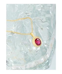 Macro shot of an oval red zircon pendant on a gold cross chain over a glass background