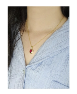 Detail shot of a minimalist gold necklace with an oval red zircon pendant on a model