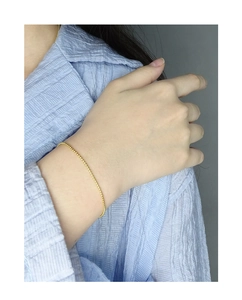 Gros plan d'un bracelet minimaliste à fines billes dorées porté au poignet élégant