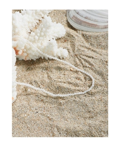Detailed shot of delicate small pearl necklace on white sand with coral and shells